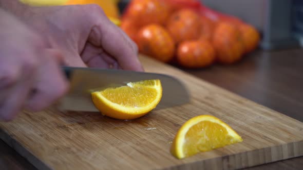 Closeup of man cutting orange into pieces on wooden chopboard alt