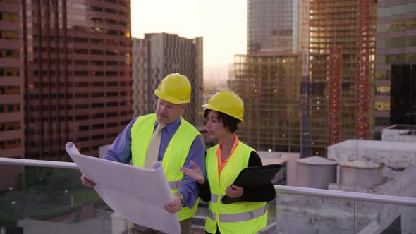 Two construction supervisors look at plans on rooftop