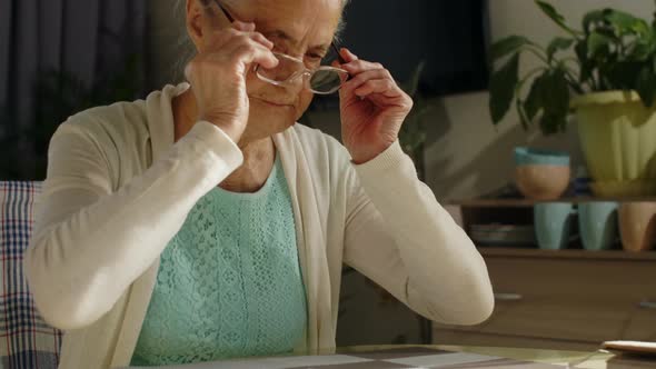 Senior Woman Putting On Glasses for Reading a Bill