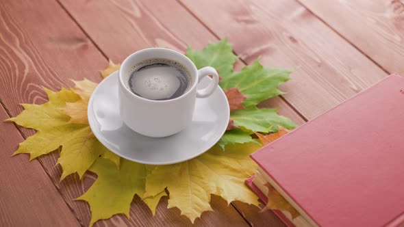 Coffe Cup on Wooden Table with Book and Colorful Autumnal Maple Leaves with Spinning Coffee Bubbles