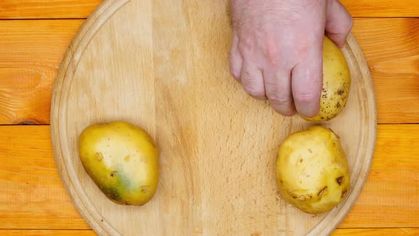 The cook is preparing to peel the potatoes. A man lays out raw fresh potatoes and a manual potato