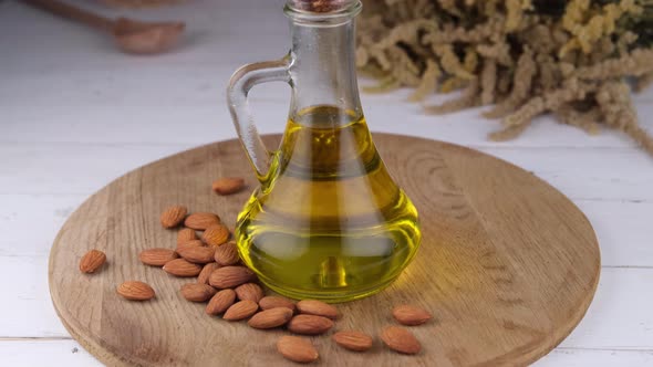 Jug or Bottle with Almond Oil on a Background of Almond Nuts on a Wooden Background alt
