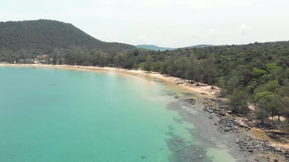 Rocky gold sandy shoreline with lush green hills encircling the shallow turquoise waters, M'pai Bay alt