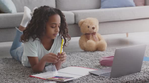 Cute African American Girl Drawing with Feltpens Lying on Floor with Laptop Watching Online Art alt