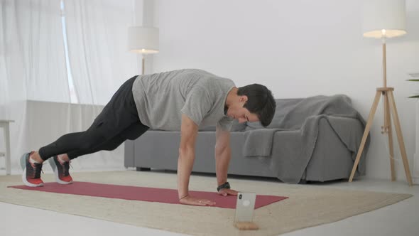 Handsome Young Man in a Gray T-Shirt and Black Shorts Does Sports at Home Online. Strong Athletic