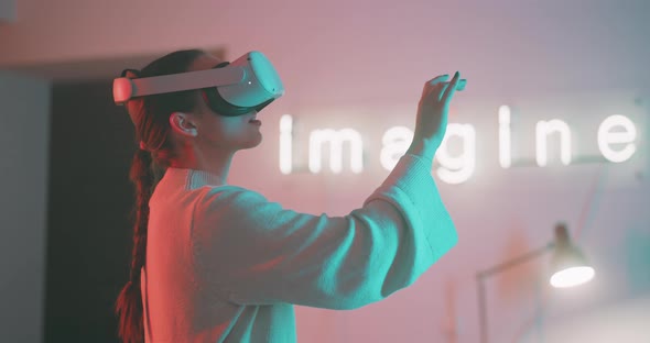 Young woman experiencing virtual reality and smiling in neon lights and sign in the background alt