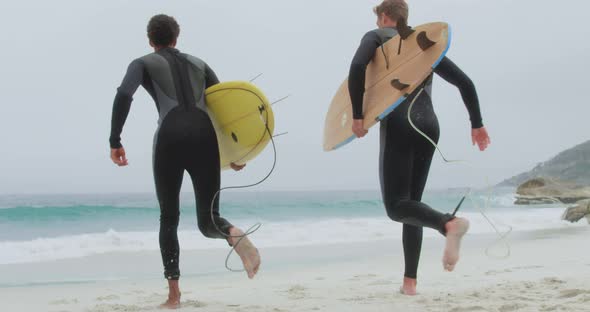 Rear view of two male surfers running together with surfboard on the beach 4k alt