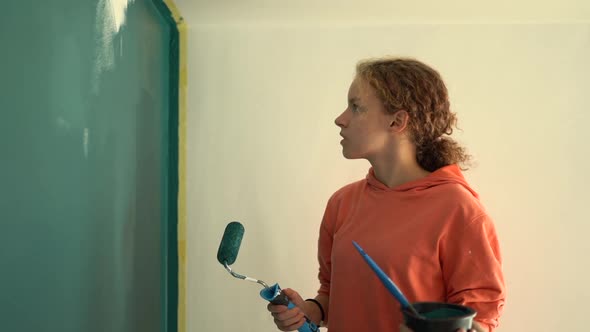 Beautiful Young Girl Paints the Wall Blue While Standing on a Stepladder alt