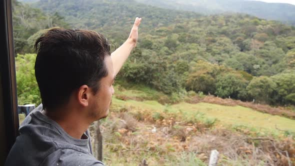 Young Man Sits in Entrance of Moving Train and Leans Out His Hand From Open Doors. Male Tourist alt
