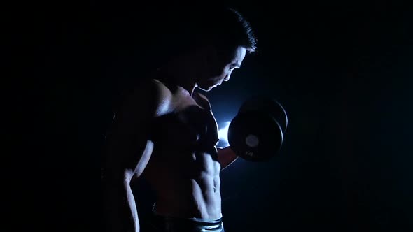 Athlete Is Training His Muscles with a Dumbbell, Black Background, Slow Motion, Silhouette alt