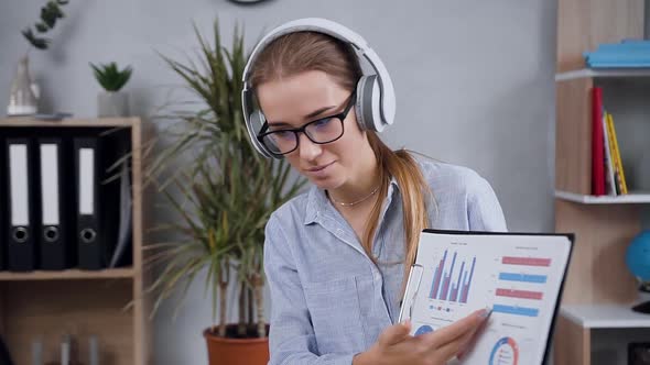 Young Woman in Headphones Having Videocall Talking with Client and Discussing Report Datas alt