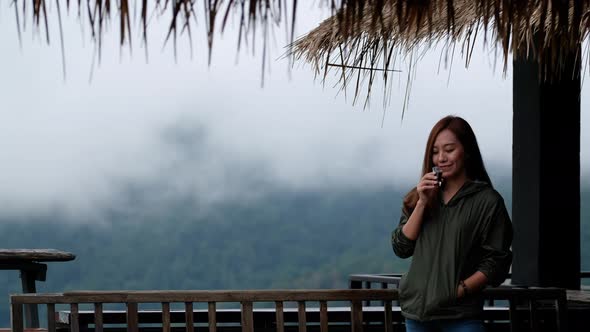 A young female traveler drinking coffee with a beautiful foggy mountain and nature view