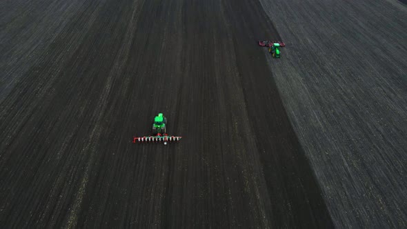 Aerial view of a two modern green tractors plowing dry agricultural field and seeding alt