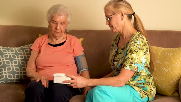 Home healthcare nurse and elderly woman taking blood pressure with a machine. alt