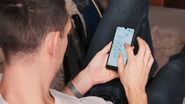 Man Looking at Map With Marked Points on Smartphone While Lying on Couch in Room alt
