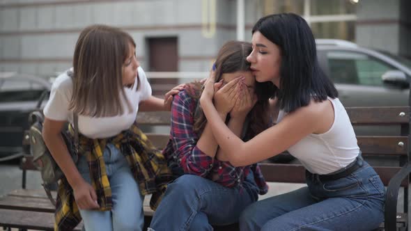 Frustrated Teenage Girl Crying As Friends Calming Down Sitting on Bench on City Street alt