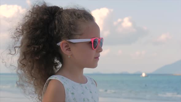 Close-up Portrait of a Beautiful Little Girl in Pink Glasses, Cute Smiling, Looking at the Sea alt