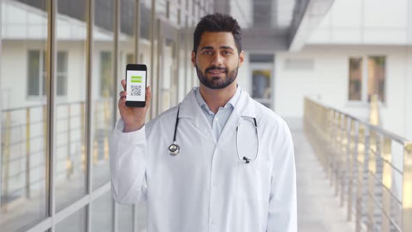 Medium Shot of Male Doctor Looking at Camera with Electronic Vaccination Certificate on Cellphone alt