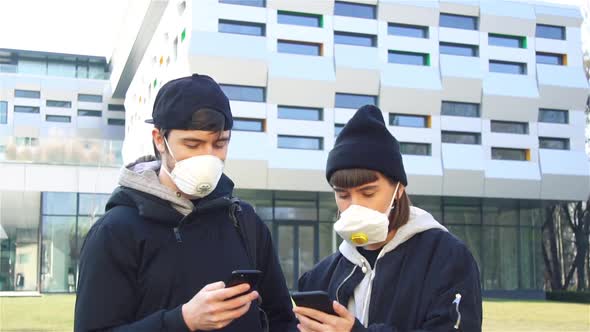 Young Couple in Respiratory Mask Using Smartphone Standing Near Modern Building