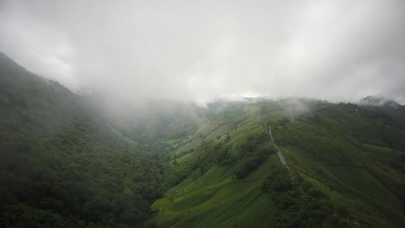 Aerial view flying above lush green tropical rain forest mountain with rain cloud cover during the r alt