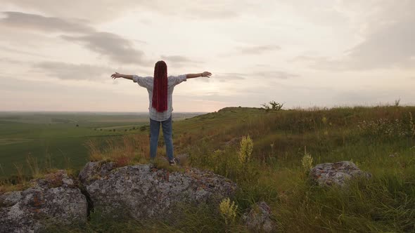 Back Side of a Girl on the Stone Raises Her Hands to the Sky alt