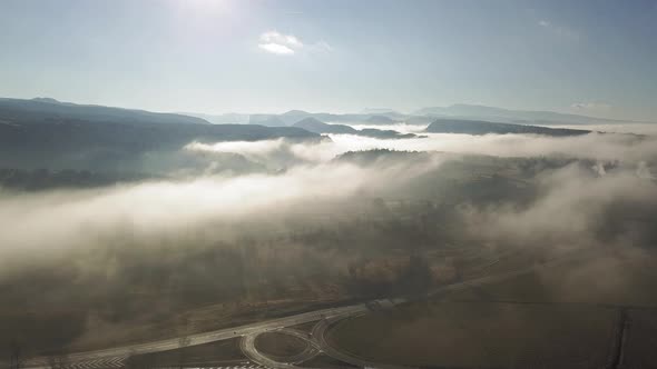 Aerial view of thick clouds of mist over rural area with road junction alt