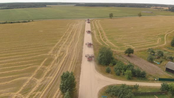 Several Combine Harvesters Move Along a Gravel Country Road in the Countryside alt