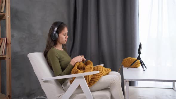 A Modern Woman in Headphones is Engaged in Knitting at Home Thanks to Sitting in a Chair and alt