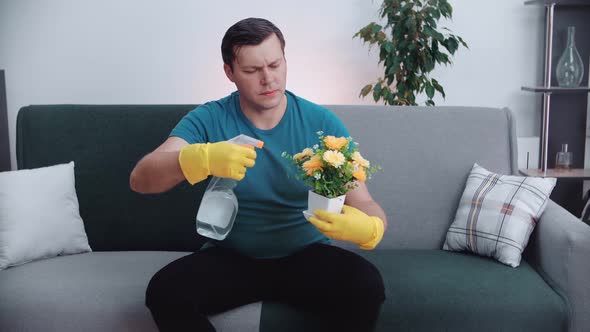 A man with a watering can watering a pot of flowers.