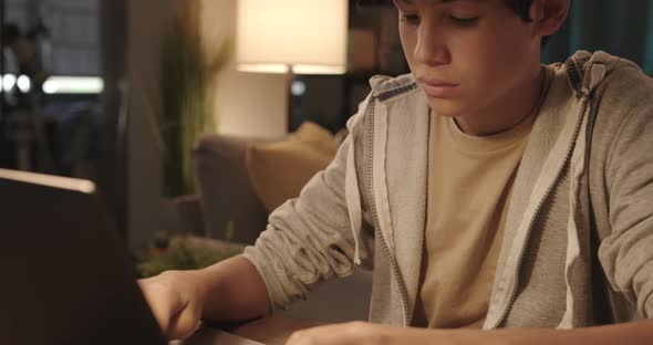 Teenager sitting at desk at home and typing with his laptop, technology and communication concept