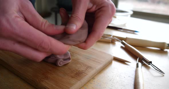 An artist pulling a piece of brown modeling clay and creating a sculpture with his hands and tools i alt