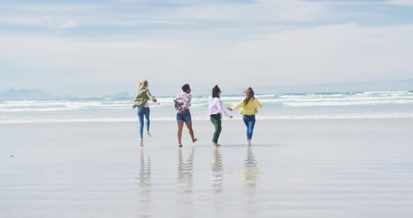 Happy group of diverse female friends having fun, running at the beach alt