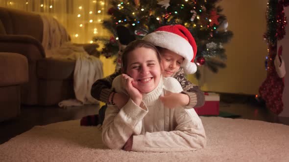 Cute Boy with Mother Relaxing on Floor and Hugging Next to Christmas Tree alt