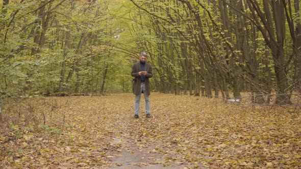 Camera Approaching To a Confident Handsome Man Standing in the Autumn Forest and Using His Tablet alt