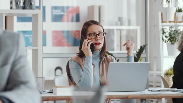 Businesswoman Talking on Phone at Desk in Open Space Office alt