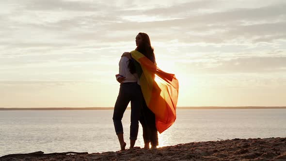 Girlfriends standing at the coast with rainbow flag.