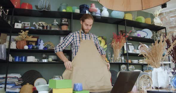 Bearded Man which Ties His Work Apron Before Starting to Work in Contemporary Handmade Gift shop alt