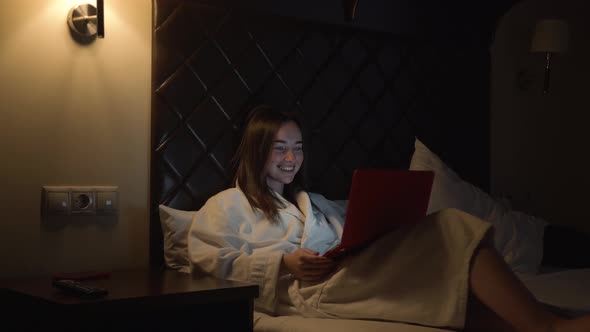 A Woman in the Evening in Bed Lies with a Laptop Speaks By Video Communication