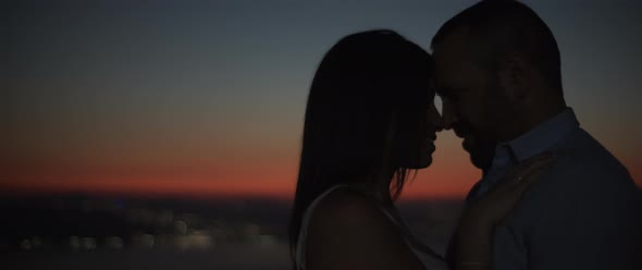 Silhouette of a couple standing close to each other, smiling, feeling happy  alt