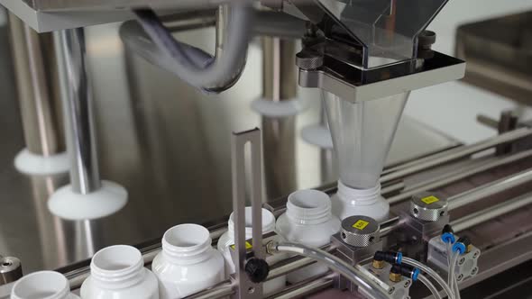 The Automated Medical Machinery is Filling the Plastic Vials with Pills Moving on the Conveyor Belt