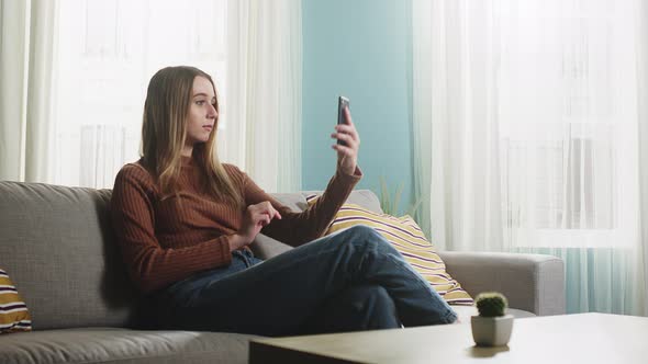 Young Girl Sitting on the Sofa with a Phone in His Hands