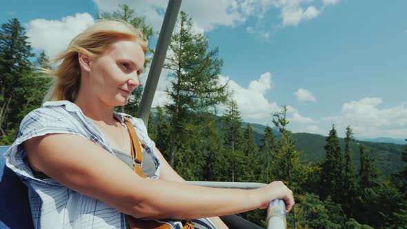 Active Woman Enjoys a Ride on a Cable Car Over a Forest Surrounded By Mountains alt