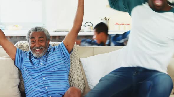 Grandfather, father and son cheering while watching tv alt
