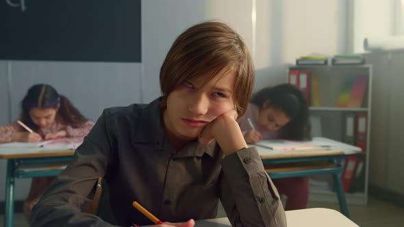 Tired Schoolboy Sitting in Classroom alt