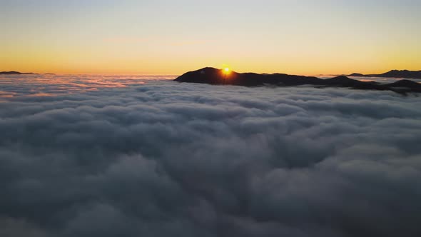 Aerial view of vibrant sunrise over white dense fog with distant dark Carpathian mountains alt