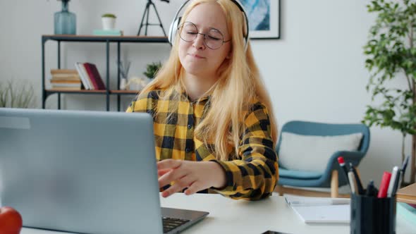 Slow Motion of Joyful Teen Using Laptop Typing and Listening To Music Wearing Headphones alt