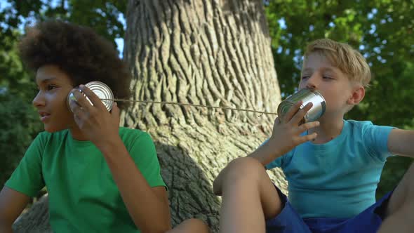 Multiracial Friends Talking Through Cans Sitting in Park, Happy Childhood, Fun