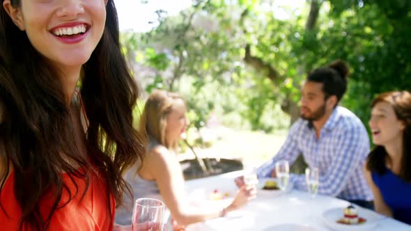 Portrait of woman standing with champagne glass while friends interacting in background alt