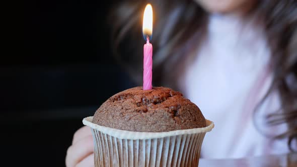 Child blows out a burning candle on a birthday cupcake. Birthday.