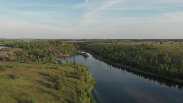 Drone flying over small lake surrounded by sparse vegetation with blue skies and white clouds alt
